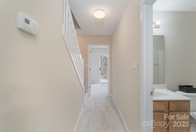 hall featuring light carpet, a sink, a textured ceiling, baseboards, and stairs