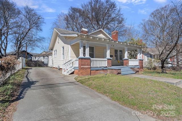 bungalow-style house featuring a chimney, covered porch, fence, driveway, and a front lawn