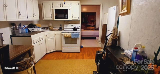 kitchen featuring black microwave, light wood-style flooring, white cabinets, electric stove, and dark countertops