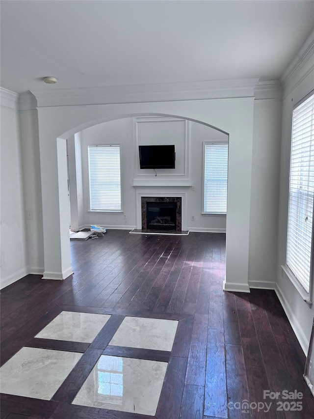 unfurnished living room with baseboards, arched walkways, hardwood / wood-style floors, crown molding, and a fireplace