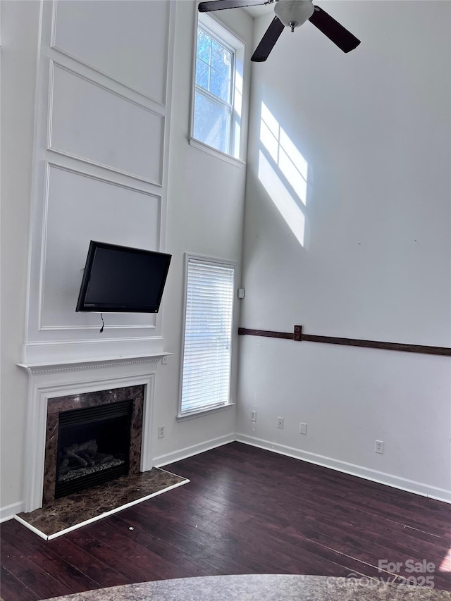 unfurnished living room with baseboards, wood finished floors, and a high end fireplace