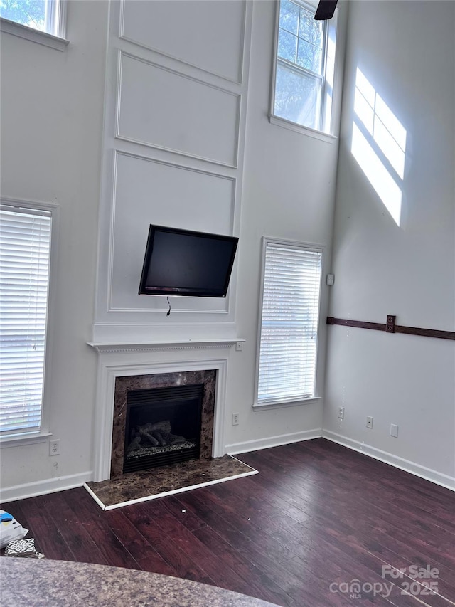 unfurnished living room with a fireplace, wood finished floors, a towering ceiling, and baseboards