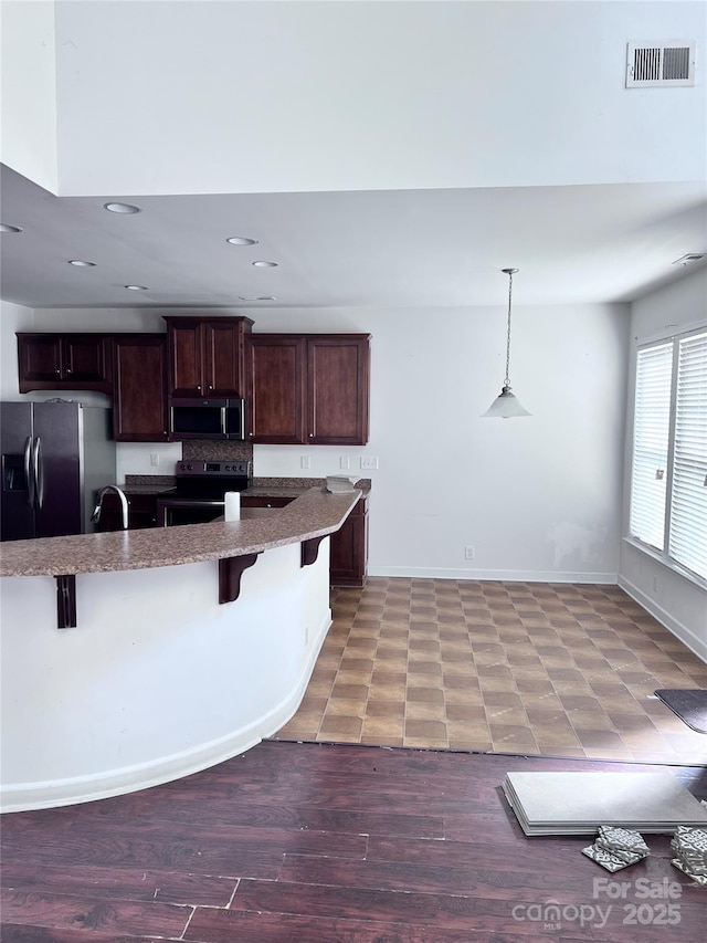 kitchen with dark brown cabinetry, visible vents, light stone counters, stainless steel appliances, and a kitchen bar