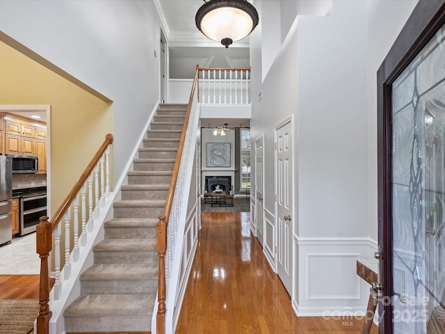 entryway featuring light wood finished floors, crown molding, wainscoting, a fireplace, and a towering ceiling