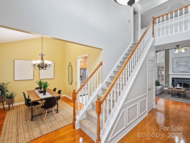 stairway featuring baseboards, a premium fireplace, an inviting chandelier, a high ceiling, and hardwood / wood-style flooring