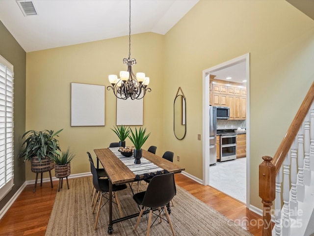 dining room featuring light wood finished floors, visible vents, a chandelier, and lofted ceiling