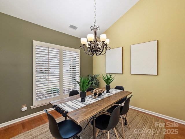 dining space with visible vents, baseboards, lofted ceiling, wood finished floors, and a notable chandelier