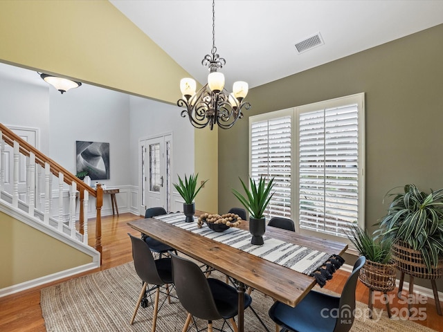 dining area with visible vents, a chandelier, stairs, lofted ceiling, and wood finished floors