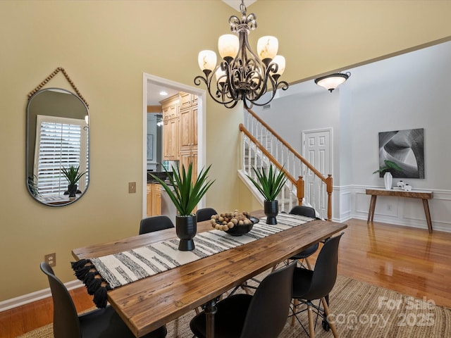 dining area with stairway, light wood-style floors, an inviting chandelier, a decorative wall, and a towering ceiling