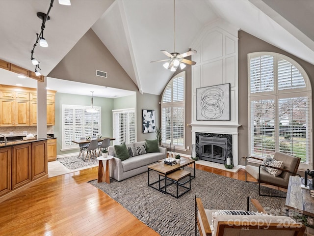 living area with light wood-style floors, visible vents, a high end fireplace, and high vaulted ceiling