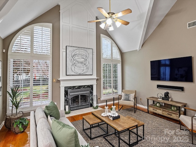 living room featuring a ceiling fan, wood finished floors, baseboards, high vaulted ceiling, and a fireplace