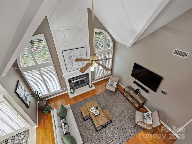 living room featuring a ceiling fan, wood finished floors, visible vents, baseboards, and lofted ceiling