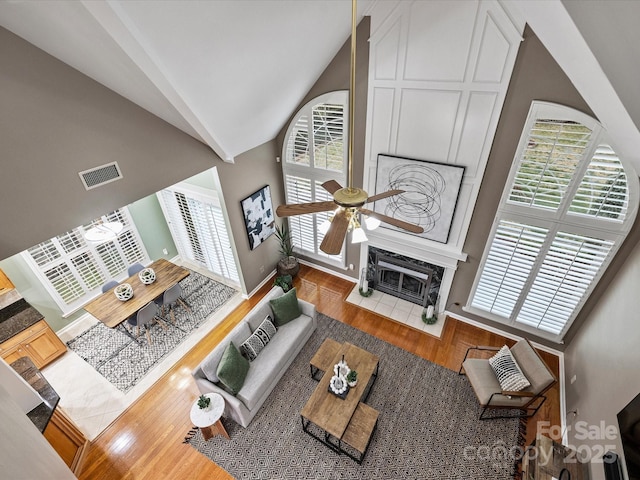 living room with wood finished floors, visible vents, a fireplace, ceiling fan, and vaulted ceiling