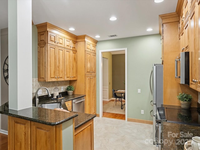 kitchen featuring dark stone countertops, visible vents, a sink, decorative backsplash, and stainless steel appliances