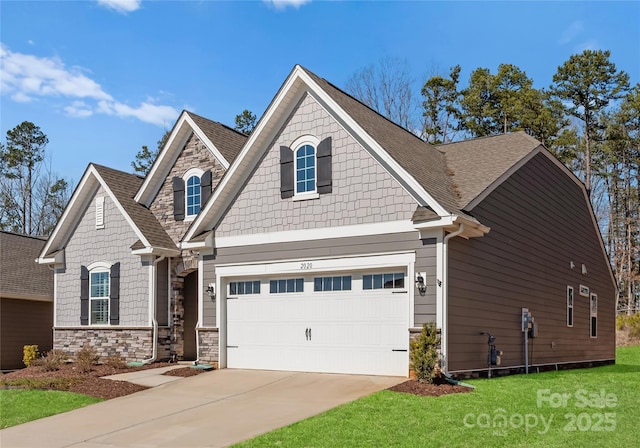 craftsman inspired home featuring an attached garage, a shingled roof, driveway, stone siding, and a front yard