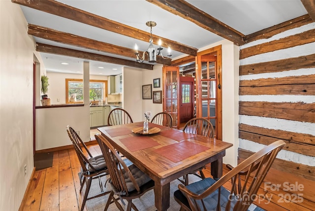 dining space with light wood-style floors, beam ceiling, a notable chandelier, and baseboards