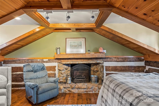 bedroom with lofted ceiling with beams, wood-type flooring, and a stone fireplace