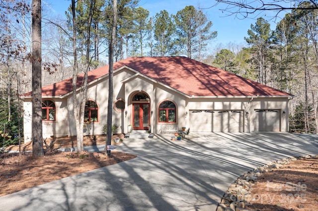 mediterranean / spanish house with driveway, french doors, an attached garage, and stucco siding