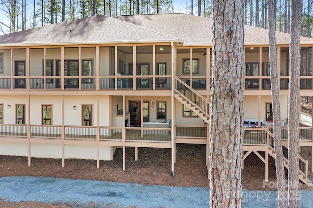 rear view of property featuring a shingled roof, stairway, and a sunroom