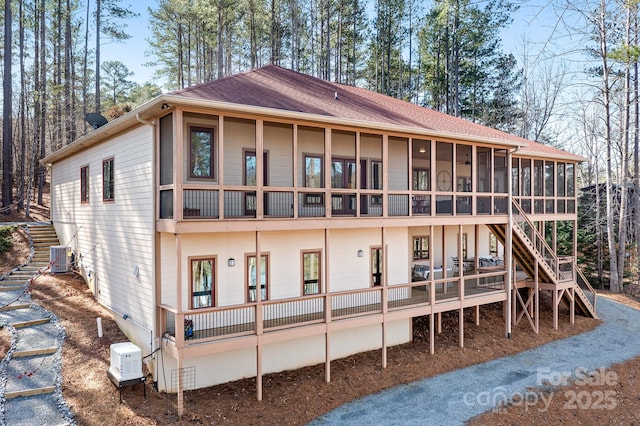 rear view of house with a shingled roof, a sunroom, stairway, and central air condition unit