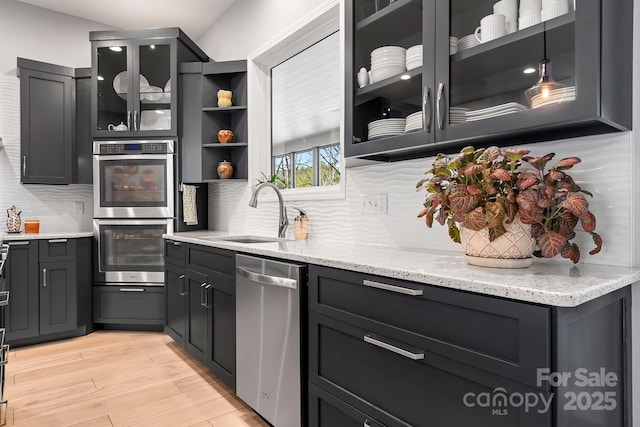 kitchen featuring light stone counters, stainless steel appliances, light wood-style flooring, decorative backsplash, and a sink