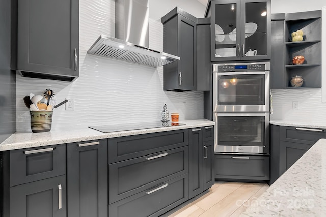 kitchen with tasteful backsplash, wall chimney exhaust hood, glass insert cabinets, black electric stovetop, and double oven