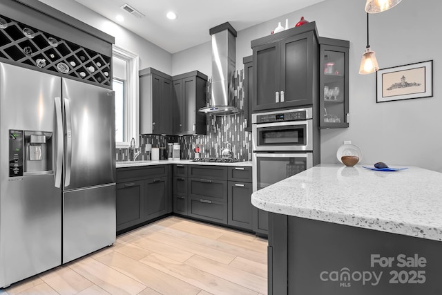 kitchen featuring visible vents, wall chimney exhaust hood, a sink, stainless steel appliances, and backsplash