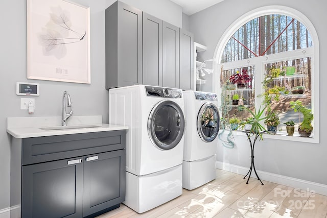 laundry room featuring cabinet space, baseboards, washing machine and clothes dryer, light wood-type flooring, and a sink