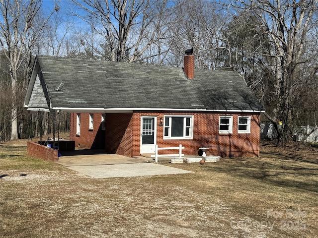 rear view of house featuring driveway, a lawn, a chimney, roof with shingles, and brick siding