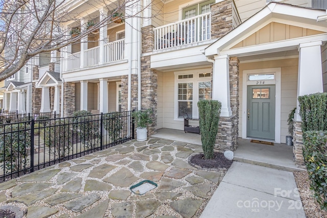 doorway to property with board and batten siding, stone siding, fence, and a porch