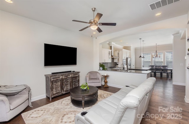 living area featuring visible vents, dark wood finished floors, baseboards, and ceiling fan with notable chandelier