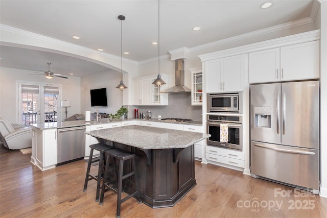 kitchen with arched walkways, stainless steel appliances, open floor plan, wall chimney range hood, and a peninsula