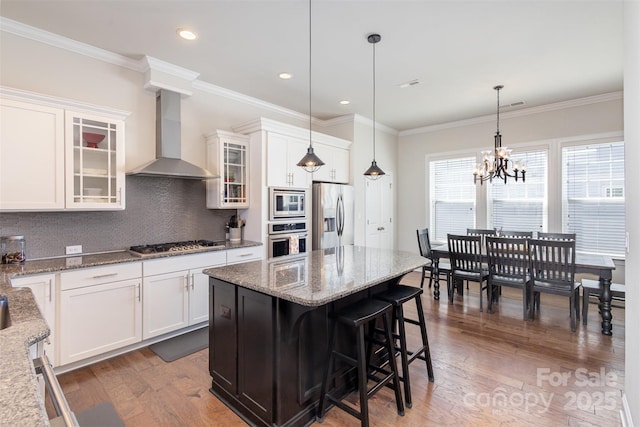 kitchen with wood finished floors, white cabinets, appliances with stainless steel finishes, wall chimney exhaust hood, and tasteful backsplash