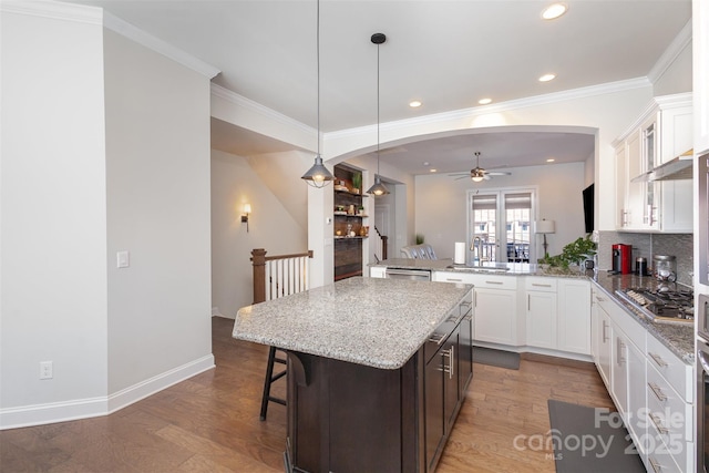 kitchen featuring arched walkways, a breakfast bar, wood finished floors, stainless steel gas cooktop, and a sink