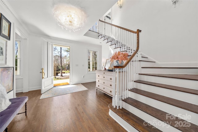 entrance foyer with baseboards, stairway, ornamental molding, wood finished floors, and an inviting chandelier