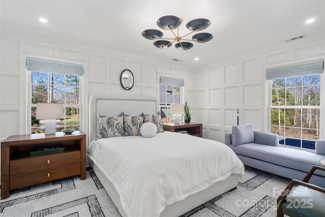 bedroom featuring multiple windows, visible vents, a decorative wall, and ornamental molding