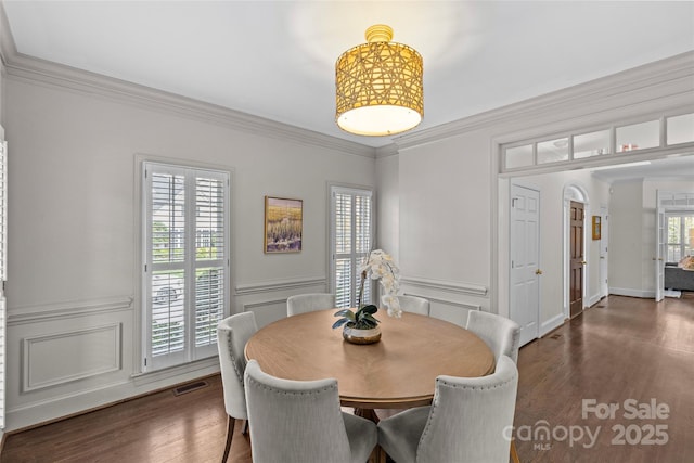 dining area with a decorative wall, visible vents, crown molding, and wood finished floors