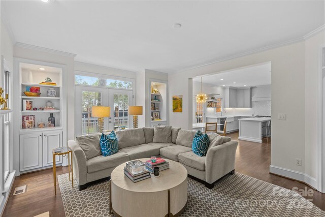 living area featuring visible vents, built in shelves, crown molding, dark wood-type flooring, and baseboards