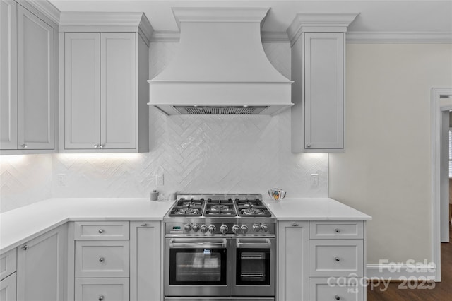 kitchen featuring light countertops, range with two ovens, premium range hood, and backsplash