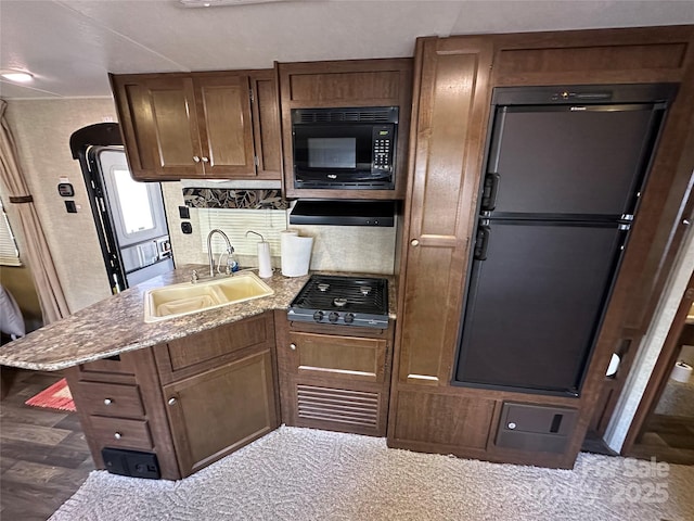 kitchen featuring light stone counters, refrigerator, gas stovetop, black microwave, and a sink