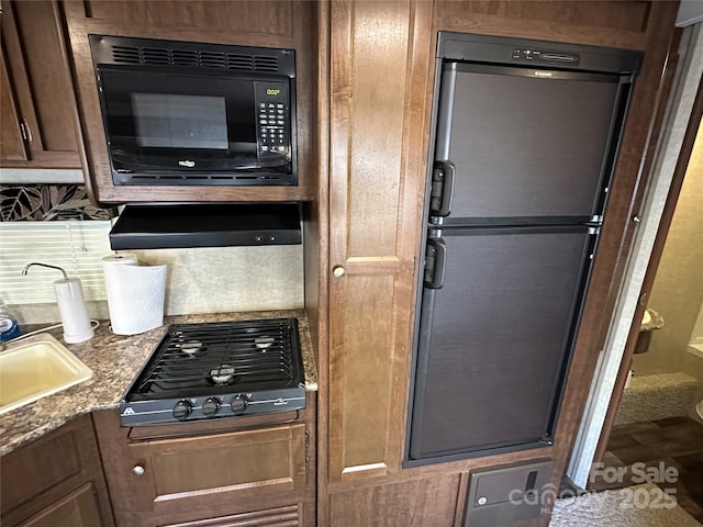 kitchen featuring gas stovetop, tasteful backsplash, freestanding refrigerator, a sink, and black microwave