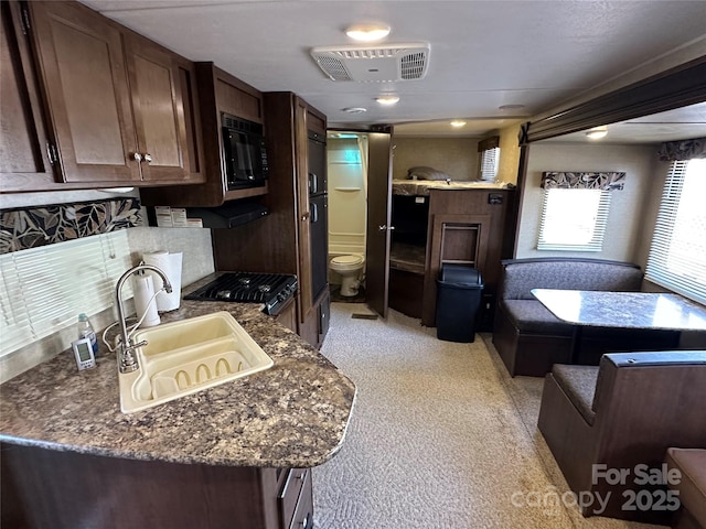 kitchen featuring black microwave, a sink, visible vents, range, and dark stone counters