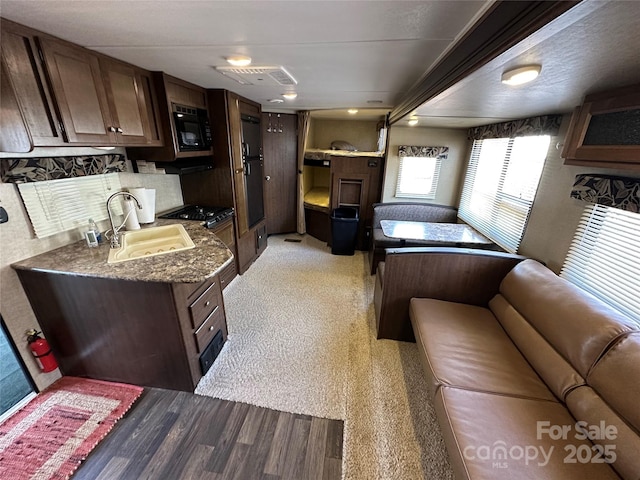 kitchen with black microwave, dark brown cabinetry, stove, a sink, and visible vents