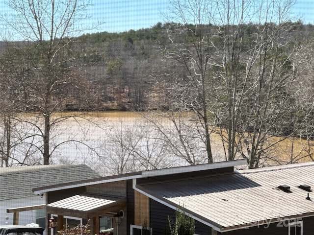 exterior space with a shingled roof and a wooded view