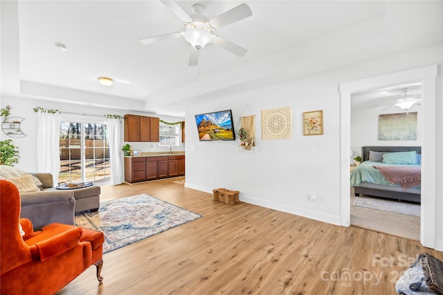 living area featuring ceiling fan, light wood finished floors, and baseboards