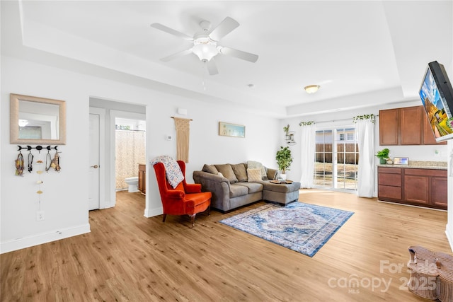 living room featuring light wood-type flooring, a raised ceiling, a healthy amount of sunlight, and baseboards