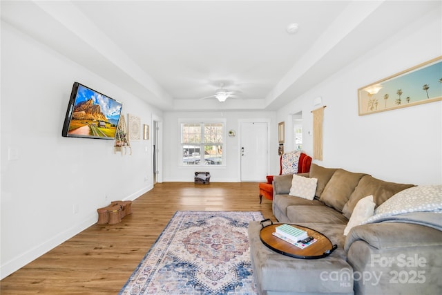 living room with a ceiling fan, a raised ceiling, light wood-style flooring, and baseboards