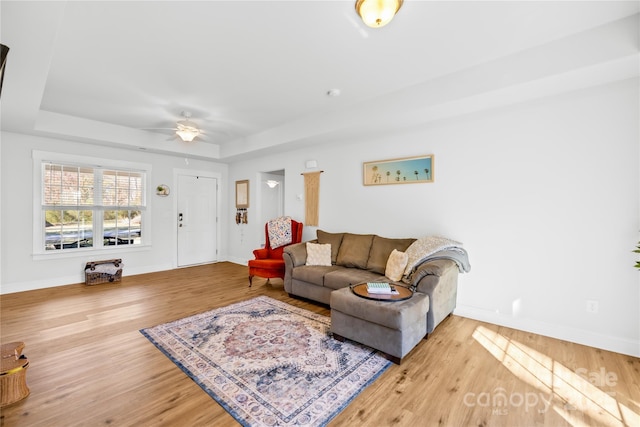 living room featuring a ceiling fan, a raised ceiling, baseboards, and wood finished floors