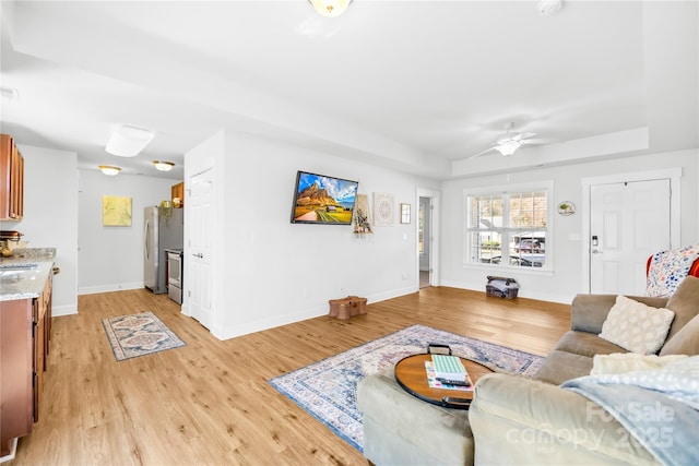 living area featuring a tray ceiling, light wood finished floors, visible vents, ceiling fan, and baseboards