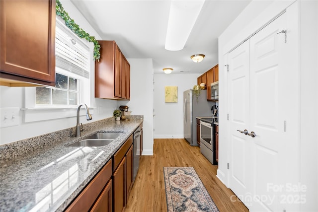 kitchen with baseboards, appliances with stainless steel finishes, light stone countertops, light wood-style floors, and a sink